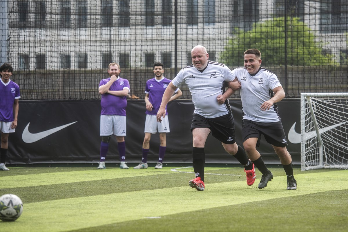 A QPR fan and Diego, a Fair Shot FC player, run with arms linked as part of a training drill