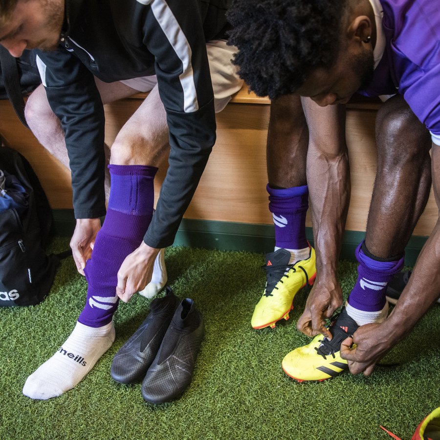 Two people put their Fair Shot FC socks on in a football changing room